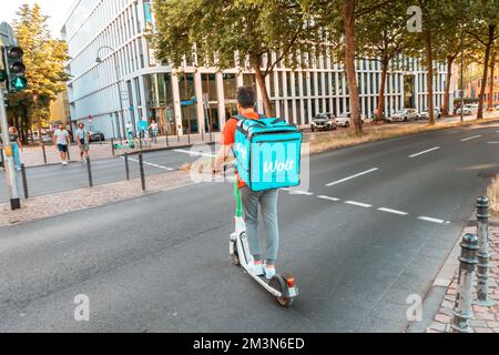 30. Juli 2022, Köln, Deutschland: Ein männlicher Wolt-Kurier auf einem Roller mit einem großen Rucksack mit Lebensmitteln führt eine Bestellung, die über eine mobile Anwendung an aufgegeben wurde Stockfoto