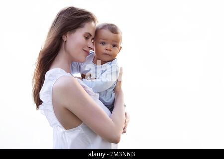 Mutter umarmt und hält das Kind in ihren Armen isoliert auf weißem Hintergrund. Eine schöne multirassische Familie Stockfoto