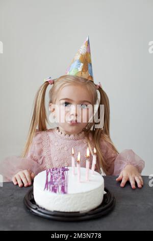 Kleines Mädchen feiert Geburtstagsparty. Blond mit langen Pferdeschwanzen Kind bläst Kerzen auf Geburtstagskuchen Stockfoto