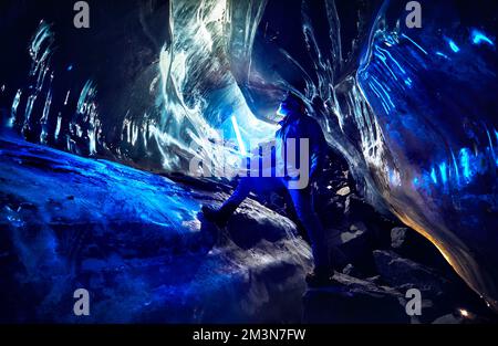 Touristen mit grauem Bart und blauem, leuchtendem LED-Licht erkunden eine fantastische Gletschereishöhle in den Bergen Kasachstans Stockfoto