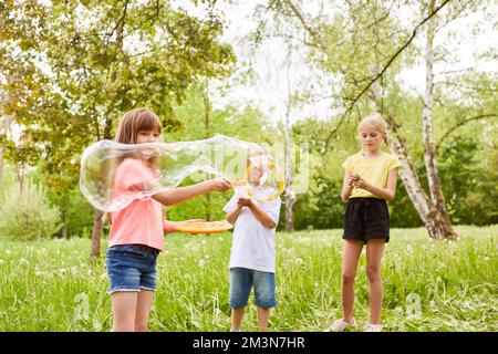 Ein Mädchen, das während des Urlaubs im Garten bei männlichen und weiblichen Freunden eine Blase durch den Zauberstab macht Stockfoto