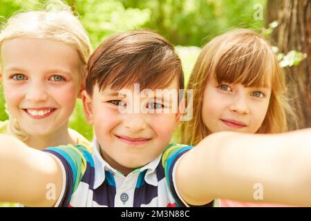 Porträt eines lächelnden Jungen, der Selfie mit Freundinnen macht, während er seine Freizeit im Garten verbringt Stockfoto