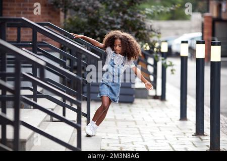 Ein afroamerikanisches Mädchen geht die Treppe auf der City Street runter. Das Porträt des Kindes im Jeansrock und T-Shirt im Freien Stockfoto