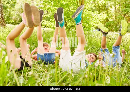 Verspielte, multirassische, männliche und weibliche Freunde mit den Beinen oben auf der Wiese während der Sommerferien Stockfoto