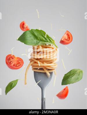 Pasta mit Tomaten und Basilikum auf einer Gabel mit schwebenden Tomaten und Basilikum Stockfoto