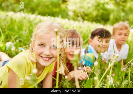 Porträt eines lächelnden Mädchens mit männlichen und weiblichen Freunden, die auf der Wiese im Garten liegen Stockfoto