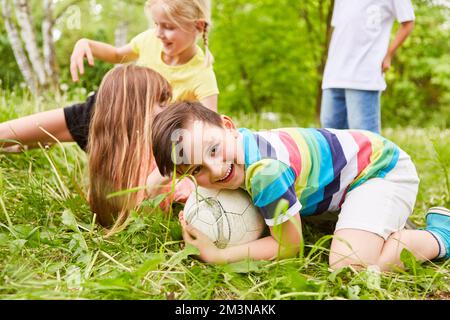 Porträt eines lächelnden Jungen, der während des Wettkampfs im Park über den Fußball krabbelt Stockfoto