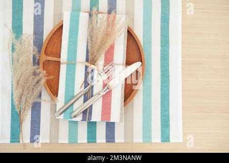 Elegante Tischgestaltung, Holzteller mit gestreifter Serviette und Besteck. Platz für Text kopieren Stockfoto