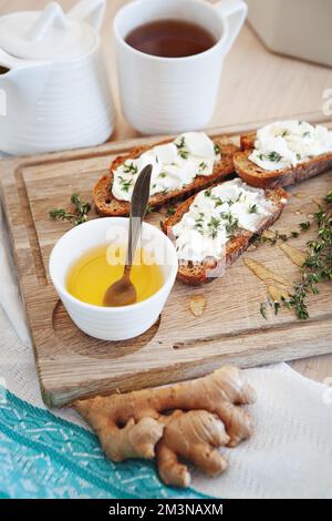 Frühstückssnacks mit einer Tasse Tee. Bruschetta mit Butter, Thymian, Ingwer und Tee mit Honig. Tischaufstellung auf Holzbrett und Stoffservietten. Tischkappe Stockfoto