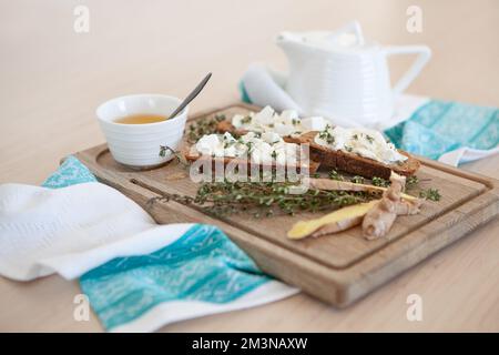 Sandwiches mit Butter, Thymian, Ingwer und Tee mit Honig. Tischaufstellung auf Holzbrett und Stoffserviette. Tischfliehen und Stillleben Stockfoto