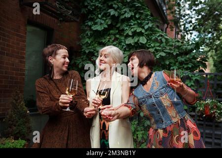 Freunde von Frauen mittleren Alters feiern, haben Spaß mit Sekt und Gläsern alkoholischen Weins oder Champagner auf einer Party im Freien Stockfoto