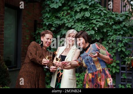 Reife Frauen feiern und lachen, halten die Wunderkerzen in der Hand und klappern Gläser alkoholischen Weins oder Champagner auf einer Party im Freien Stockfoto