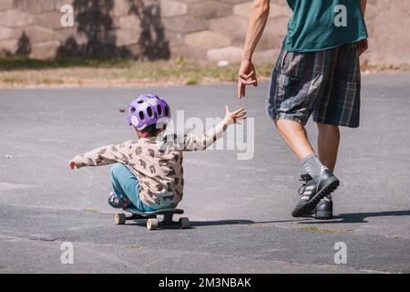 30. Juli 2022, Köln, Deutschland: Ein Vater bringt seinem Sohn Skateboard bei. Vaterschaft, Sport und Freizeit zusammen mit der Familie Stockfoto