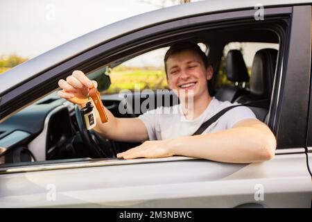 Anfänger, die Autoschlüssel aus dem Fenster halten und lächeln. Konzept für einen neuen Fahrer auf der Straße. Stockfoto