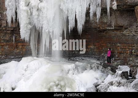 Ashgill Force, Garrigill, Cumbria, Großbritannien. 16.. Dezember 2022 Wetter in Großbritannien. Ein Wanderer genießt das Spektakel der riesigen Eiszapfen, die nach einer weiteren Nacht unter den Temperaturen in Cumbria vom gefrorenen Wasserfall der Ashgill Force in der Nähe von Garrigill hängen. Kredit: David Forster/Alamy Live News Stockfoto