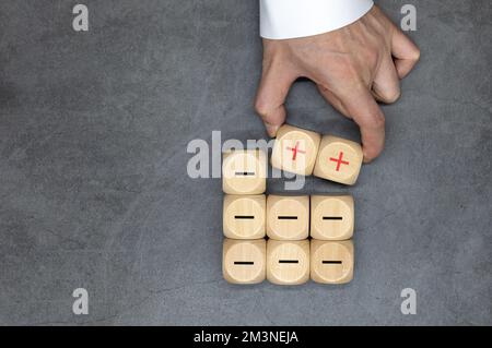 Plus- und Minus-Symbole auf Holzwürfeln. Trennen Sie das Negative vom Positiven, entfernen Sie die Schwächen oder Negativität, positives Denken, negatives Feedback Stockfoto