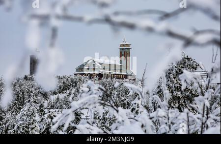 Oberwiesenthal, Deutschland. 16.. Dezember 2022. Blick durch schneebedeckte Bäume bis zum Gipfel des Fichtelbergs mit dem Fichtelberghaus. Die Saison beginnt am selben Tag im größten alpinen Skigebiet Sachsens. Vor allem der Frost der letzten Nächte hatte den Betreibern der Fichtelberg-Seilbahn in die Karten gespielt. So könnte man ausreichend künstlichen Schnee mit 70 Schneekanonen herstellen. Die ersten Langlaufstrecken sind ebenfalls in Betrieb. Kredit: Jan Woitas/dpa/Alamy Live News Stockfoto