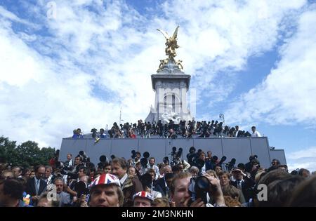 Menschenmassen vor dem Buckingham Palace am Hochzeitstag von Prinz Andrew, Herzog von York, und Lady Sarah Ferguson am 23. Juli 1986 warten auf das Auftauchen der frisch Vermählten und der königlichen Familie auf dem Balkon des Palastes. Blick aus der Fischperspektive mit der Victoria Memorial Statue in der Mitte des Bildes. Datum: 1986 Stockfoto