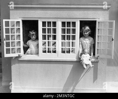 Bezauberndes Foto von Prinzessin Elizabeth (Königin Elizabeth II) und ihrer jüngeren Schwester Prinzessin Margaret, die an den Fenstern von y Bwthyn bach to Gwellt (das walisische Cottage) posiert, einem Spielzeughaus, das Prinzessin Elizabeth zum sechsten Geburtstag von den Menschen von Wales geschenkt wurde. Datum: c.1933 Stockfoto