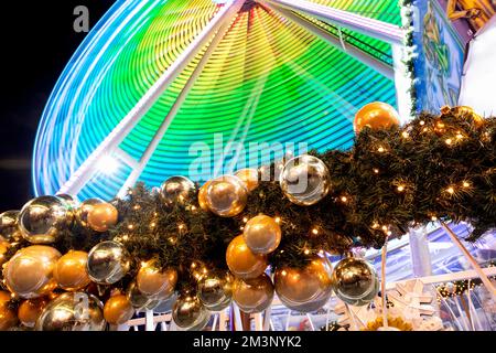 Nahaufnahme des Weihnachtsbaums mit vielen goldenen silbernen Schüsseln Dekoration deutscher Weihnachtsmarkt Platz vor hell beleuchtetem Riesenrad Stockfoto