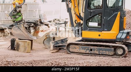 Kleiner Bagger, der auf einer Baustelle an der Straße der Stadt arbeitet. Ausrüstung, Arbeit und Beschäftigung in der Industrie Stockfoto