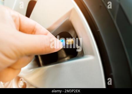 Der Fahrer setzt die Ventilkappe des Radreifens eines Fahrzeugs auf, nachdem er das Fahrzeug aufgepumpt hat, Fahrzeugbauteilkonzept Stockfoto