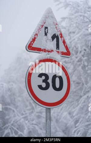 Nahaufnahme der Verkehrsschilder Geschwindigkeitsbegrenzung 30 km Verschneite Auffahrt. Winterwald nach Schneefall. Stockfoto
