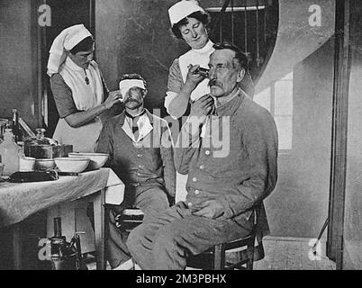 Zwei britische Krankenschwestern, die dem St. Johns freiwillige Hilfseinheit bei der Betreuung von zwei französischen Soldaten. Einer trägt einen Verband auf das Auge des Soldaten auf, während der andere einem zweiten Soldaten Antiseptikum ins Ohr spritzt. Datum: 1916 Stockfoto
