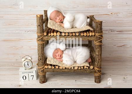 Winzige neugeborene Zwillinge in weißen Bodys mit hellem Holzhintergrund. Stockfoto