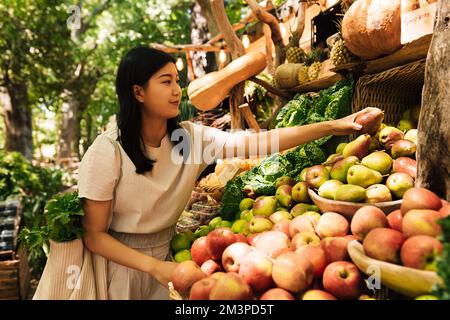 Eine Frau, die Obst auf einem Straßenmarkt kauft. Asiatische Frau, die auf einem Bauernmarkt Obst aussucht. Stockfoto