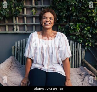 Glückliche reife Frau auf einer Bank. Mittelalterliche Frau mit kurzen Haaren, die draußen lacht. Stockfoto