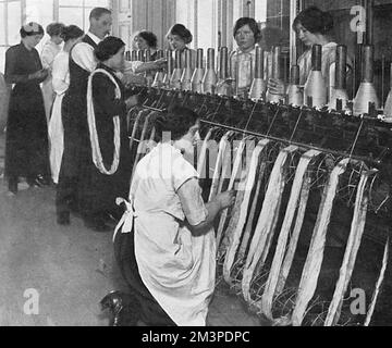 Die Arbeit der Königin für den Frauenfonds, dessen Hauptquartier in einer Villa in Piccadilly lag, wurde mit nur einigen der siebzig Maschinen abgebildet, die im Salon installiert waren, um an etwa zwei Millionen Socken zu arbeiten, die für die Soldaten an der Front benötigt wurden. Datum: 1915 Stockfoto