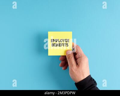 Die männliche Hand hält ein gelbes Haftpapier mit dem Wort "Mitarbeiterleistungen". Von Arbeitgebern an Arbeitnehmer gezahlte Entschädigung. Stockfoto