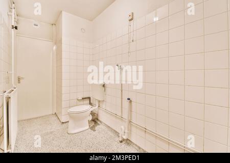 Ein Badezimmer mit weißen Fliesen an den Wänden und eine Toilette in der Ecke neben der Duschkabinentür Stockfoto