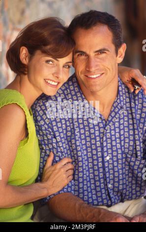 Ein jüngeres Paar mittleren Alters posierte lächelnd vor der Kamera. Die Frauen sind bei ihrem Mann Stockfoto