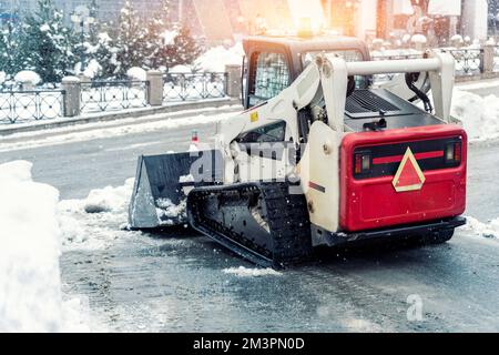 Skistraktoren-Ladermaschine reinigen schmutzigen Schnee auf der Fahrbahn. Die Straßen der Stadt säubern, Schneeeis bei schweren Schneefällen und Schneestürmen entfernen. Schneepflug Stockfoto