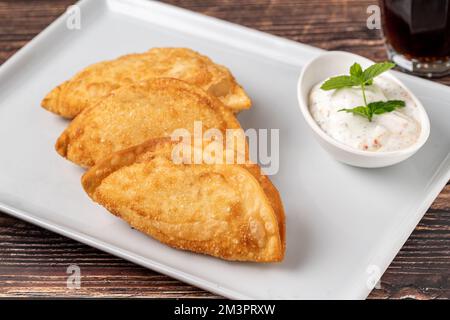 Rindercheburek auf einem Holztisch. Frittierte Beef Teigtaschen mit Fleisch und Zwiebeln. Türkischer Name CI Borek oder Cig Borek Stockfoto