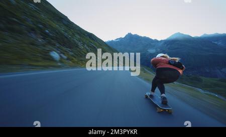 Downhill-Longboard-Session im Kino. Junge Frau, die Skateboarden fährt und zwischen den Kurven auf einem Bergpass Tricks macht. Konzept des Extremsports Stockfoto