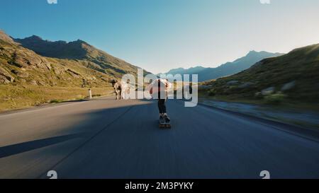 Downhill-Longboard-Session im Kino. Junge Frau, die Skateboarden fährt und zwischen den Kurven auf einem Bergpass Tricks macht. Konzept des Extremsports Stockfoto