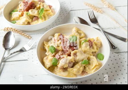 Cremige Tortellini mit Parmesankäse und italienischem Schinken auf weißem Hintergrund Stockfoto