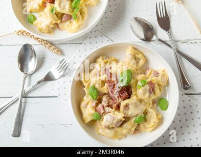 Tortellini alla Panna traditionell hausgemacht. Serviert auf weißen Tellern auf weißem Hintergrund. Flach verlegt Stockfoto