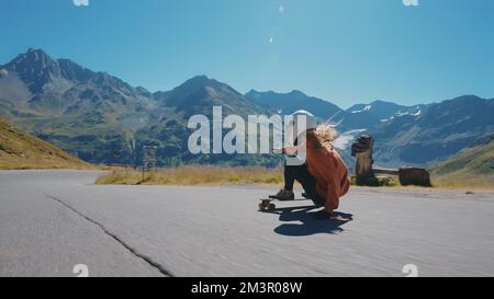 Downhill-Longboard-Session im Kino. Junge Frau, die Skateboarden fährt und zwischen den Kurven auf einem Bergpass Tricks macht. Konzept des Extremsports Stockfoto