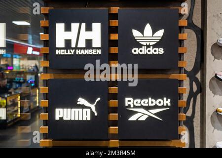 Logos beliebter Schuh- und Bekleidungsmarken im Inneren eines Markengeschäfts - Adidas, Reebok, Puma, Helly Hansen. Stockfoto