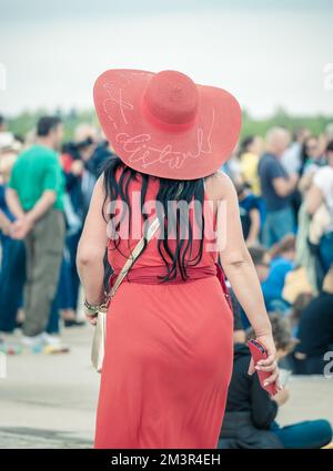 Rückansicht mit einer nicht identifizierten Frau in einem roten Kleid und einem großen Sonnenhut auf dem Kopf. Stockfoto