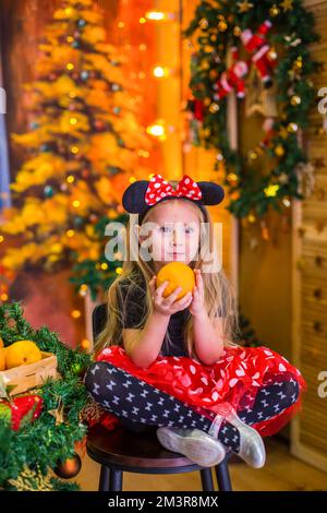 Ein Mädchen im Silvesterkostüm an einem Tisch mit Mandarinen Stockfoto