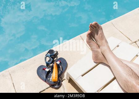 Beine in der Nähe der Brille mit Lotion Flip Flops in der Nähe des Pools, Auflösung und qualitativ hochwertiges, wunderschönes Foto Stockfoto