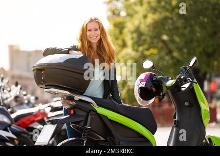 Rothaarige Frau auf ihrem Motorrad auf einem Parkplatz, die in die Kamera schaut Stockfoto