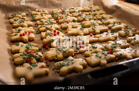 Blick aus der Nähe auf ein Tablett mit frisch gebackenen, hausgemachten weihnachtskeksen, kleine Figuren, dekoriert mit Zuckerüberzug und bunten Zuckerperlen, Bac Stockfoto