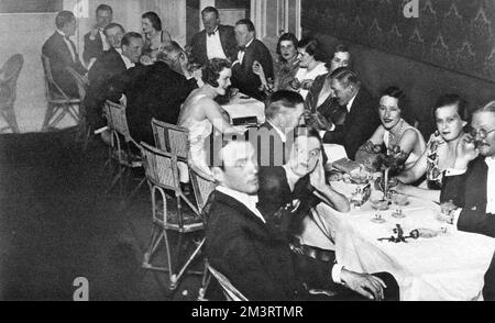 Gruppen, die sich unterhalten und Gesichter beim Abendessen im neu eröffneten Embassy Club in Kairo ziehen. Am Ende des Tisches stehen Miss Margaret Whigham (später Mrs. Charles Sweeny, dann Herzogin von Argyll) und der Graf von Warwick. Margaret und der Earl, eine beliebte Debütantin, verloben sich während ihres Aufenthalts in Kairo, zu viel Aufregung in den Klatschspalten, aber sie beendete es später nur ein paar Wochen vor der Hochzeit. Datum: 1932 Stockfoto