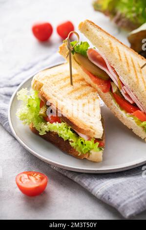 Club-Sandwich auf einem Teller mit Schinken, Käse, Gurken, Tomaten und Salatblättern aus nächster Nähe auf blauem Hintergrund mit Mayonnaise. Stockfoto